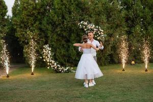 il primo danza di il sposo e sposa nel un' corto nozze vestito su un' verde prato foto