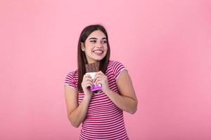 bello sorridente adolescenziale ragazza mangiare cioccolato. Immagine di contento carino giovane donna in piedi isolato al di sopra di rosa sfondo mangiare cioccolato. foto