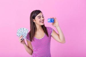 bellissimo giovane casuale bionda ragazza in piedi isolato al di sopra di rosa sfondo, mostrando plastica credito carta e i soldi banconote foto