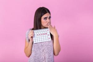 ritratto di un' bellissimo giovane ragazza Tenere sua mestruazione calendario e copertura sentire viso isolato al di sopra di rosa sfondo. periodo calendario foto