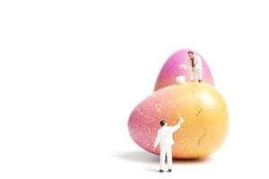 persone in miniatura che dipingono le uova di Pasqua per il giorno di Pasqua su uno sfondo bianco