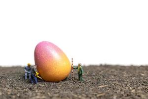 persone in miniatura che lavorano su uova di Pasqua per il giorno di Pasqua con uno sfondo bianco foto