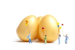 persone in miniatura con palloncini che celebrano la Pasqua su uno sfondo bianco