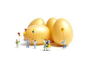 persone in miniatura in possesso di palloncini che celebrano la Pasqua su uno sfondo bianco foto