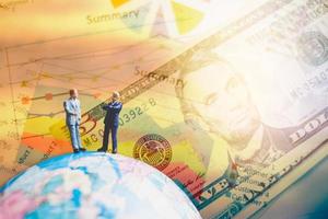 persone in miniatura in piedi su una mappa del mondo globo con grafici e banconote in dollari per la finanza e il concetto di business foto