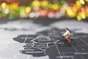 viaggiatore in miniatura in sella a una bicicletta su una mappa del mondo, viaggiando ed esplorando il concetto di mondo foto