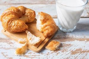 croissant su un tagliere di legno accanto al bicchiere di latte sul tavolo di legno blu foto