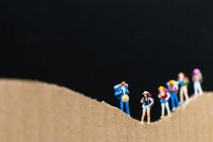 viaggiatori in miniatura con zaini che camminano su una montagna di carta, viaggio e concetto di trekking