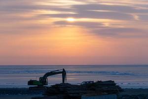 escavatore su una riva vicino al corpo d'acqua contro un colorato tramonto nuvoloso a vladivostok, russia foto