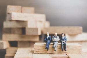 uomini d'affari in miniatura seduti su un blocco di legno con uno sfondo di legno