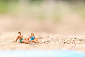 persone in miniatura che indossano costumi da bagno rilassante su una spiaggia, concetto di estate foto