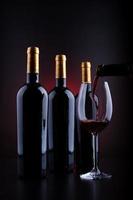 bottiglie di vino e bicchiere pieno con sfondo rosso e nero foto