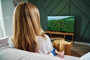 donna interruttore canali su tv impostato con a distanza controllo. foto