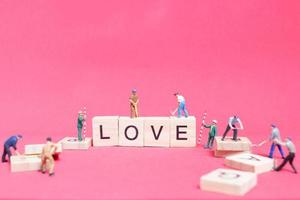 lavoratori in miniatura che costruiscono la parola amore su blocchi di legno con uno sfondo rosa, concetto di San Valentino foto