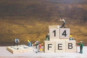 lavoratori in miniatura che costruiscono le parole e le date per il giorno di San Valentino su blocchi di legno con fondo in legno, concetto di San Valentino