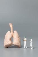 medici e infermieri in miniatura che osservano e discutono del concetto di polmone umano, virus e batteri