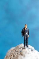 uomo d'affari in miniatura in piedi su una roccia con uno sfondo blu foto