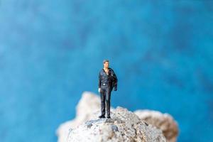 uomo d'affari in miniatura in piedi su una roccia con uno sfondo blu foto