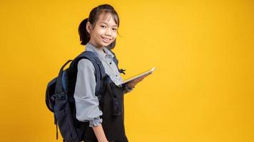 giovane ragazza asiatica che indossa uno zaino e tenendo tablet guardando la telecamera con sfondo giallo