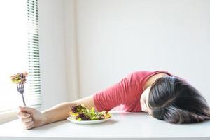 donna con piatto di insalata con la testa posa sul tavolo da pranzo accanto alla finestra luminosa