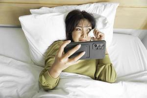 un' triste giovane asiatico donna è pianto al di sopra di sua Telefono mentre dire bugie su il letto foto