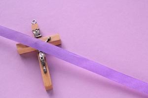 cristiano religioso di legno attraversare crocifisso con viola nastro su viola sfondo. cattolico religione simbolo. bene venerdì, prestato stagione, palma domenica, cenere mercoledì e santo settimana concetto foto