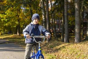 un' allegro cinque anni ragazzo cavalcate un' bicicletta nel un autunno cappello e giacca contro il sfondo di autunno alberi foto