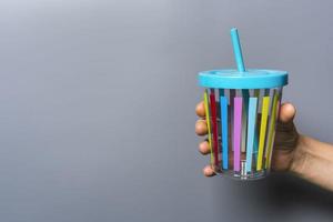 un' colorato succo tazza con un' cannuccia nel un' donna di mano su un' grigio sfondo, donna mano Tenere un' tazza foto