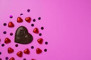 cioccolato cuore e molte di brillante caramella nel il forma di cuori avvolto nel Foglio su un' rosa sfondo foto