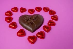un' grande cioccolato cuore e un' lotto di brillante caramella nel il forma di cuori avvolto nel Foglio foto