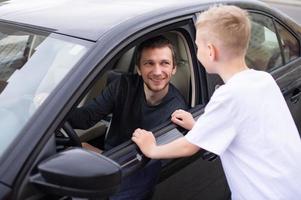 un' carino bambino accompagna un' contento padre per opera. papà è seduta nel il auto foto