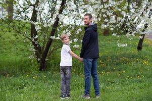 papà detiene il del bambino mano e essi camminare attraverso il fioritura giardino foto