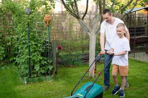 papà e il suo curioso figlio falciare il verde prato vicino il Casa. foto