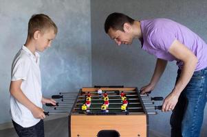 carino ragazzo giocando tavolo calcio con il suo emotivo papà nel il camera foto