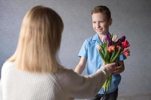 carino ragazzo sorridente e dando fiori per mamma per compleanno foto