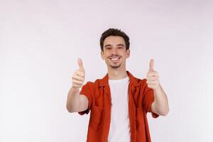 ritratto di contento sorridente giovane uomo mostrando pollici su gesto e guardare a telecamera su isolato al di sopra di bianca sfondo foto