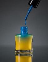 fluente blu chiodo polacco nel un' giallo bottiglia isolato su nero foto