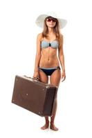 pieno lunghezza ritratto di un' bellissimo giovane donna in posa nel un' bikini, cappello e occhiali da sole con un' valigia nel mano su bianca foto