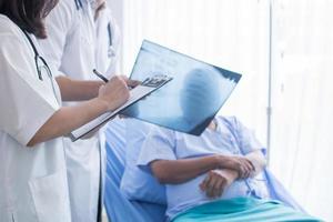 medici che scrivono su carta e che esaminano una radiografia accanto a un paziente