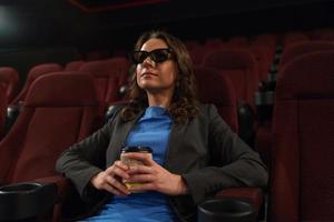 giovane donna orologi film 3d a il cinema e bevande caffè, guardare a il schermo foto