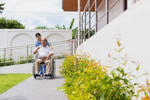 assistenza infermieristica casa cura concetto. asiatico giovane infermiera Disabilitato anziano uomo. infermiera, cura casa e anziano uomo con invalidità nel un' sedia a rotelle nel un al di fuori medico facilità. foto