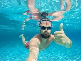 barba uomo con bicchieri immersione nel un' blu pulito acqua con pollice su foto