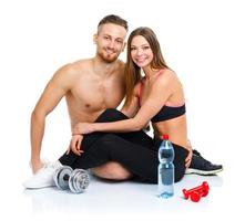 atletico coppia - uomo e donna dopo fitness esercizio con manubri e bottiglia di acqua seduta su il bianca foto