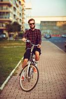 uomo nel occhiali da sole equitazione un' bicicletta su città strada foto