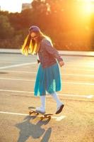 bellissimo giovane donna con skateboard, retroilluminato a tramonto foto