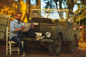 giovane elegante uomo con bicchieri e arco cravatta vedere il carta geografica vicino il vecchio stile suv foto