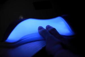 vista del primo piano delle mani femminili con manicure con smalto gel. la donna mette la mano nella lampada uv a led per polimerizzare la copertura superiore dello smalto. lampada uv, chiodo a led foto