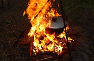 cucinando all'aperto nel campo condizioni. calderone su un' fuoco nel il foresta. cucinando a il palo mentre in viaggio. tripode con un' giocatore di bowling cappello su un' fuoco su picnic. concettuale viaggiare, il trekking e avventura foto