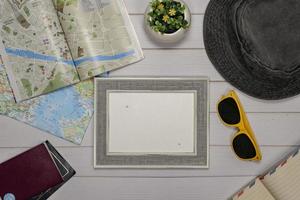 viaggio piatto posare di un vuoto telaio, occhiali da sole, passaporto, telecamera e un' carta geografica al di sopra di un' bianca di legno tavolo foto