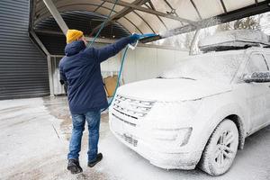 uomo lavaggio americano suv auto con tetto cremagliera a un' se stesso servizio lavare nel freddo tempo atmosferico. foto